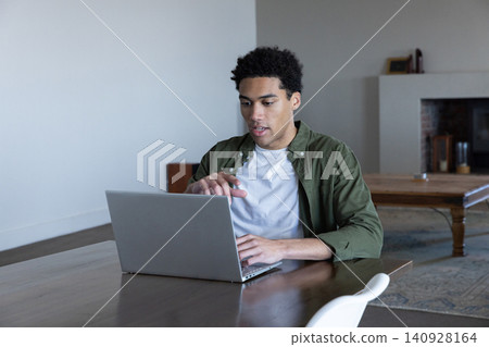 African american man typing on laptop at table gesturing toward display in living room African american man typing on laptop at table gesturing toward display in living room 140928164