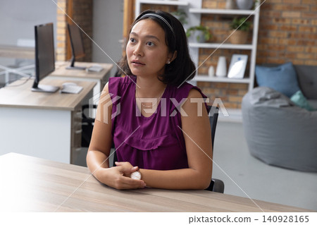 Asian woman gazing upward at desk in office with monitors Asian woman gazing upward at desk in office with monitors 140928165
