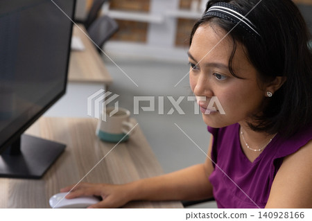 Asian woman working on computer using mouse at desk with coffee mug, copy space Asian woman working on computer using mouse at desk with coffee mug, copy space 140928166