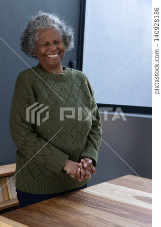 Senior african american woman standing beside table under window wearing sweater laughing Senior african american woman standing beside table under window wearing sweater laughing 140928186