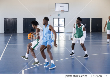 African american men dribbling orange basketball on polished court at gym with basketball hoop African american men dribbling orange basketball on polished court at gym with basketball hoop 140928193