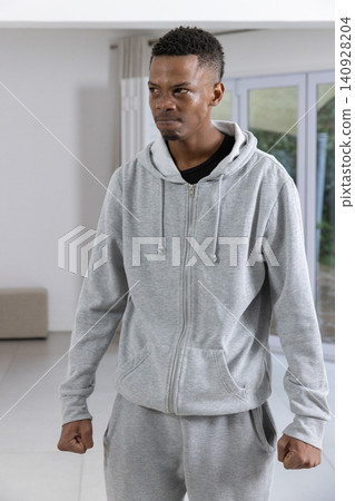 African american man standing at home in grey hoodie and sweatpants near sliding doors African american man standing at home in grey hoodie and sweatpants near sliding doors 140928204