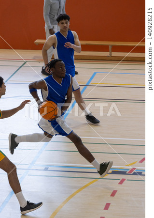 Diverse male basketball players playing fast-paced game on gym court with basketball Diverse male basketball players playing fast-paced game on gym court with basketball 140928215