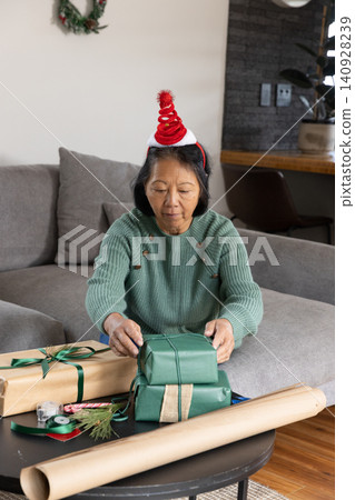 Senior Asian woman with red headband wrapping presents at black coffee table in living room Senior Asian woman with red headband wrapping presents at black coffee table in living room 140928239