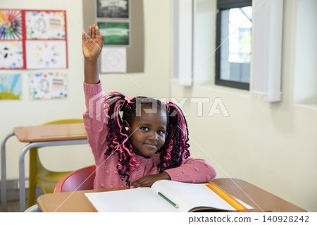 African american girl student sitting at desk at school and writing in open notebook with pencils African american girl student sitting at desk at school and writing in open notebook with pencils 140928242