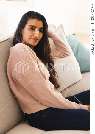 Asian woman leaning back on sofa with pillows in living room wearing pink top and jeans Asian woman leaning back on sofa with pillows in living room wearing pink top and jeans 140928270