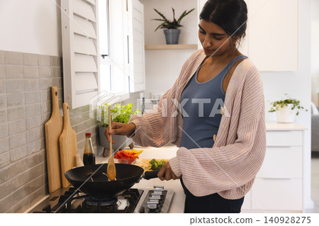 Asian woman stirring wok pan on gas burner in home kitchen near cutting board, copy space Asian woman stirring wok pan on gas burner in home kitchen near cutting board, copy space 140928275