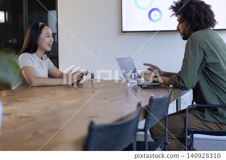 Diverse coworkers collaborating on laptop and smartphone at conference table, display screen Diverse coworkers collaborating on laptop and smartphone at conference table, display screen 140928310