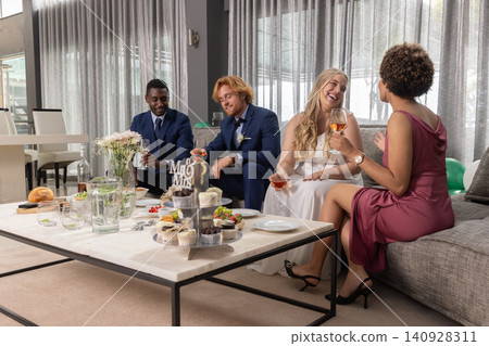 Diverse wedding party holding wine glasses near cupcake stand, chatting at reception lounge Diverse wedding party holding wine glasses near cupcake stand, chatting at reception lounge 140928311