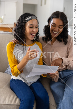 Woman explaining paperwork as teenage daughter reacting on sofa at home Woman explaining paperwork as teenage daughter reacting on sofa at home 140928327