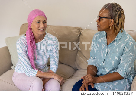 Diverse female friends sitting on couch in living room discussing support with headscarf, pillow 140928337