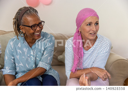 Diverse senior friends chatting on couch in living room with green cushion, pink balloons Diverse senior friends chatting on couch in living room with green cushion, pink balloons 140928338