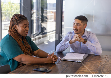 Diverse coworkers in business attire discussing project at conference table with laptop Diverse coworkers in business attire discussing project at conference table with laptop 140928339