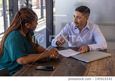 Diverse coworkers discussing printed document at table in glass-door meeting area Diverse coworkers discussing printed document at table in glass-door meeting area 140928342