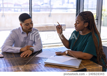 Diverse team sitting at office table holding pencil, reviewing documents near laptop, smartphone Diverse team sitting at office table holding pencil, reviewing documents near laptop, smartphone 140928343