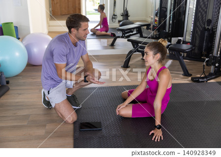 Fitness instructor kneeling coaching client sitting on mat in gym with tablet, stability balls 140928349