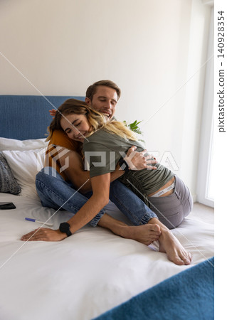 Couple embracing on bright bed in bedroom at home with pregnancy test, tv remote and potted plant Couple embracing on bright bed in bedroom at home with pregnancy test, tv remote and potted plant 140928354