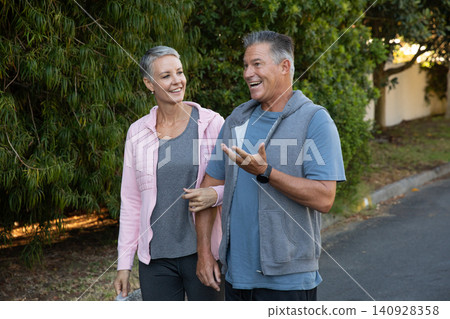 Senior couple walking on suburban street in activewear, holding water bottle, wearing smartwatch Senior couple walking on suburban street in activewear, holding water bottle, wearing smartwatch 140928358