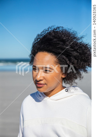 African american woman wearing white hooded sweatshirt, gazing at ocean waves on sandy beach 140928365