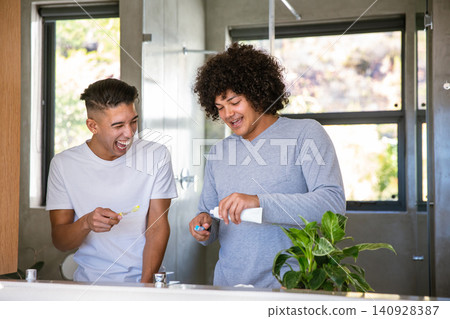 Diverse male friends brushing teeth with toothbrushes and toothpaste tube by bathroom sink Diverse male friends brushing teeth with toothbrushes and toothpaste tube by bathroom sink 140928387