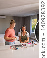 Diverse female duo demonstrating eyeshadow palettes on table in bedroom with ring light, brushes 140928392