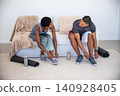 Diverse friends sitting on living room sofa tying sneaker laces near mats and water bottles 140928405