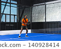African American man in his 20s holding padel racket preparing serve on blue synthetic turf court 140928414