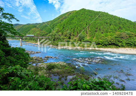 A diesel railcar on the Yodo Line crosses the First Shimanto River Bridge, overlooking the emerald-colored Shimanto River. 140928478