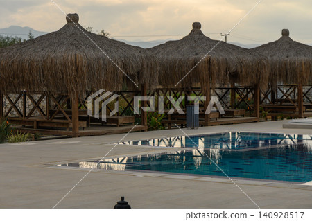 Tranquil poolside retreat with thatched umbrellas at a serene resort in the late afternoon light Tranquil poolside retreat with thatched umbrellas at a serene resort in the late afternoon light 140928517