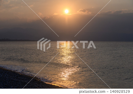 Golden sunset reflects on tranquil waters, enveloping the shoreline in a warm glow near the mountains Golden sunset reflects on tranquil waters, enveloping the shoreline in a warm glow near the mountains 140928529