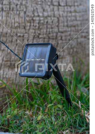 Solar-powered garden light shining brightly in a tranquil green landscape near a rustic tree 140928549