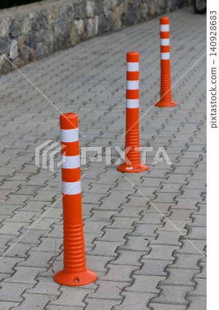 Bright orange traffic cones align on a patterned street, guiding vehicles and pedestrians in a busy urban setting during daylight hours Bright orange traffic cones align on a patterned street, guiding vehicles and pedestrians in a busy urban setting during daylight hours 140928683
