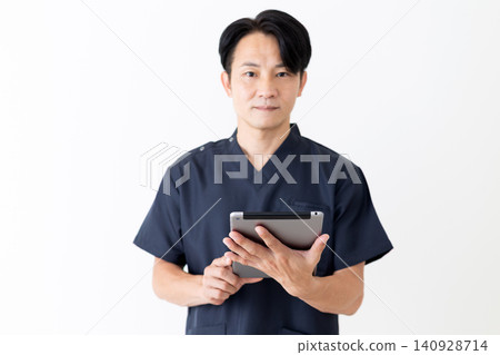 A middle-aged male doctor in navy blue scrubs holding a tablet. 140928714