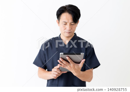 A middle-aged male doctor in navy blue scrubs holding a tablet. A middle-aged male doctor in navy blue scrubs holding a tablet. 140928755