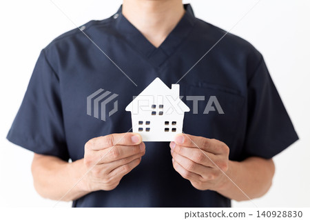 一位身穿藏藍色手術服的中年男醫生，手裡拿著一個房屋模型。 140928830