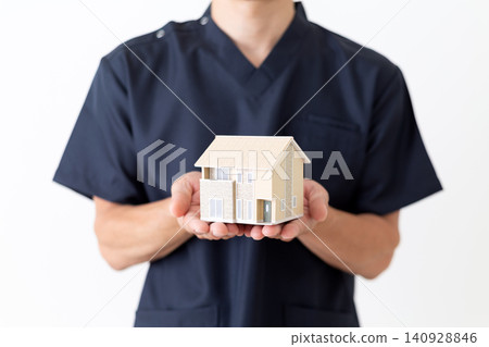 A middle-aged male doctor in navy blue scrubs holding a model house. 140928846
