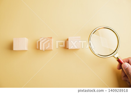 Three wooden blocks on yellow background with magnifying glass. 140928918