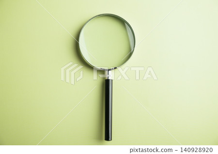 A magnifying glass with a black handle on a light green background. A magnifying glass with a black handle on a light green background. 140928920