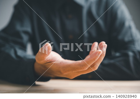 Sign of an offering, a closeup man hand pose gesture shows an open palm, a universal sign for help, charity, or receiving something with a dark blurred background indoors Sign of an offering, a closeup man hand pose gesture shows an open palm, a universal sign for help, charity, or receiving something with a dark blurred background indoors 140928940