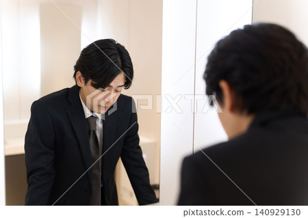 一名亞洲男子在浴室鏡子前檢視自己的臉部表情。 140929130