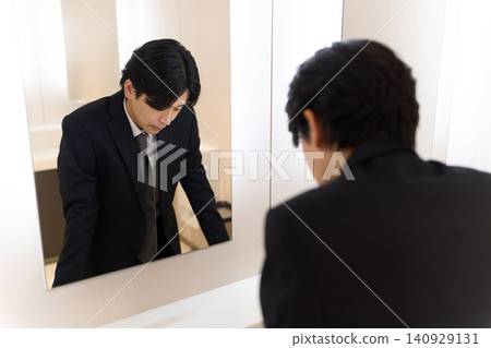 An Asian man checks his facial expression in the bathroom mirror. An Asian man checks his facial expression in the bathroom mirror. 140929131