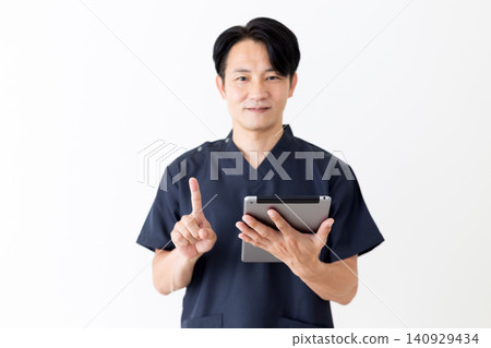 一位身穿藏藍色手術服的中年男醫生舉起平板電腦,豎起食指。 一位身穿藏藍色手術服的中年男醫生舉起平板電腦,豎起食指。 140929434