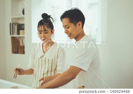 A couple enjoying cooking in a bright kitchen, both smiling. A couple enjoying cooking in a bright kitchen, both smiling. 140929486