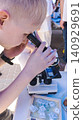 Curious boy looking through a microscope at an outdoor science fair. Enthusiastic kid exploring biology sample during an educational laboratory festival. Curious boy looking through a microscope at an outdoor science fair. Enthusiastic kid exploring biology sample during an educational laboratory festival. 140929691