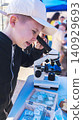 Curious boy looking through a microscope at an outdoor science fair. Enthusiastic kid exploring biology sample during an educational laboratory festival. Curious boy looking through a microscope at an outdoor science fair. Enthusiastic kid exploring biology sample during an educational laboratory festival. 140929693
