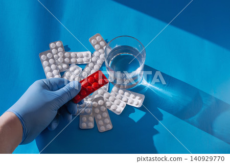 Medical glove holding red blister pack with pills and water. Medical glove holding red blister pack with pills and water. 140929770