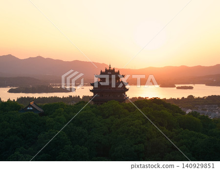 Traditional Chinese Chenghuang pagoda stands silhouetted against the orange sunset sky above West Lake and distant mountains in Hangzhou, China Traditional Chinese Chenghuang pagoda stands silhouetted against the orange sunset sky above West Lake and distant mountains in Hangzhou, China 140929851