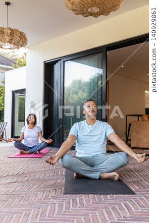 Mature man and senior woman meditating on covered patio outside sliding glass doors on yoga mats Mature man and senior woman meditating on covered patio outside sliding glass doors on yoga mats 140929861