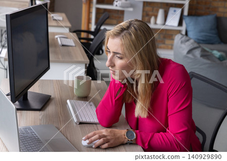 Woman leaning forward at desk using wireless mouse and laptop, magenta blouse and coffee mug Woman leaning forward at desk using wireless mouse and laptop, magenta blouse and coffee mug 140929890