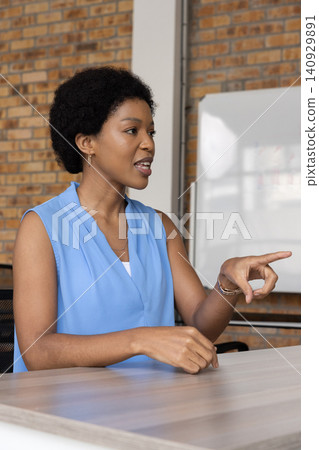 African American woman speaking and pointing at conference table with whiteboard and sleeveless top 140929891